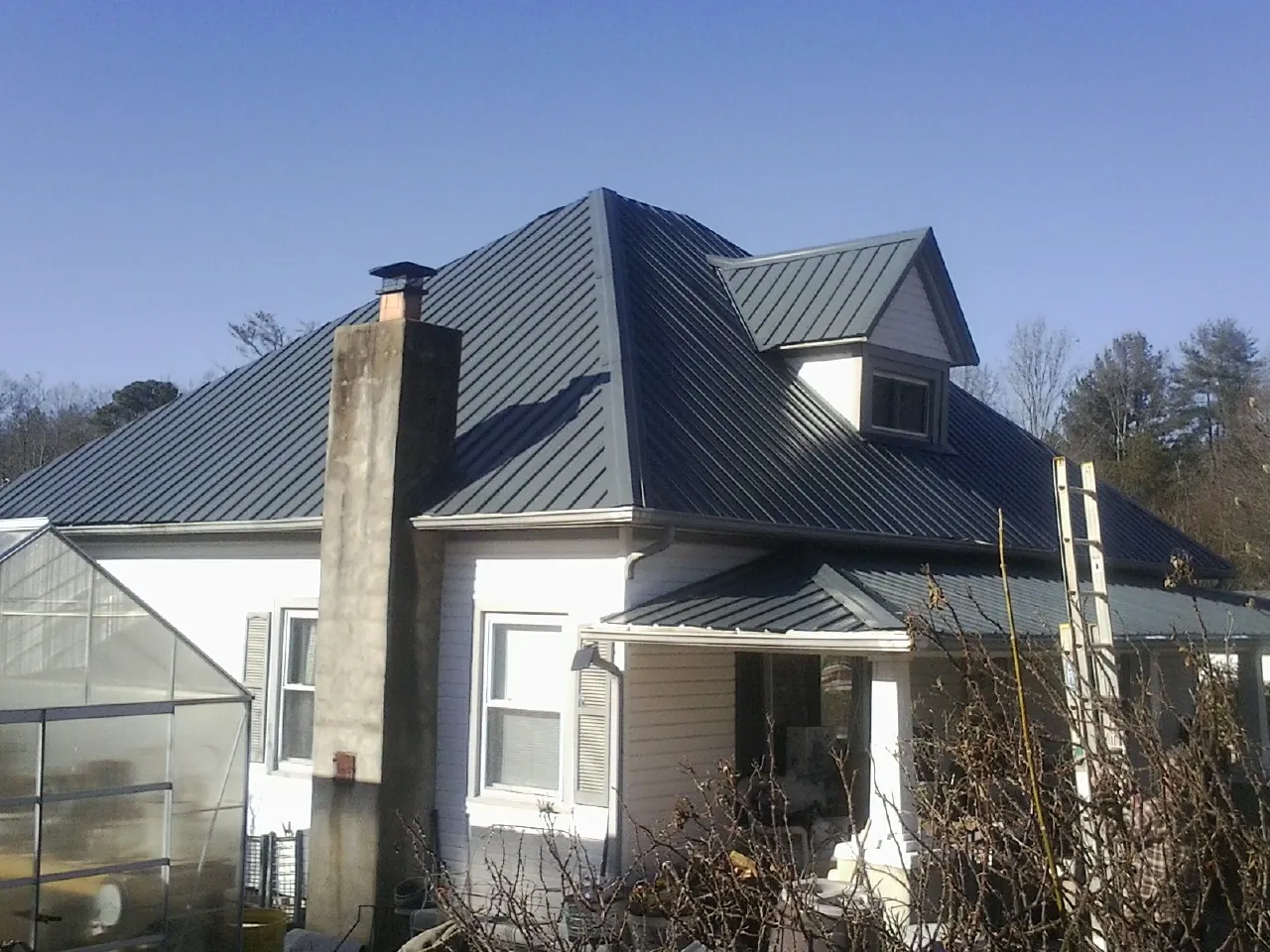 Dark blue standing seam metal roof on a white farmhouse with dormer — Slate & Tile Roof Repair by Roofing Brothers in Horseheads