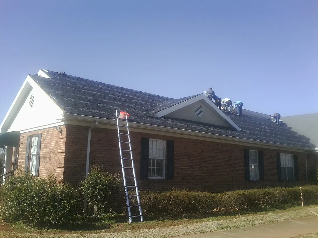 Crew tearing shingles off a brick ranch roof with a ladder set — Metal Roof Repair work by our crew in Horseheads