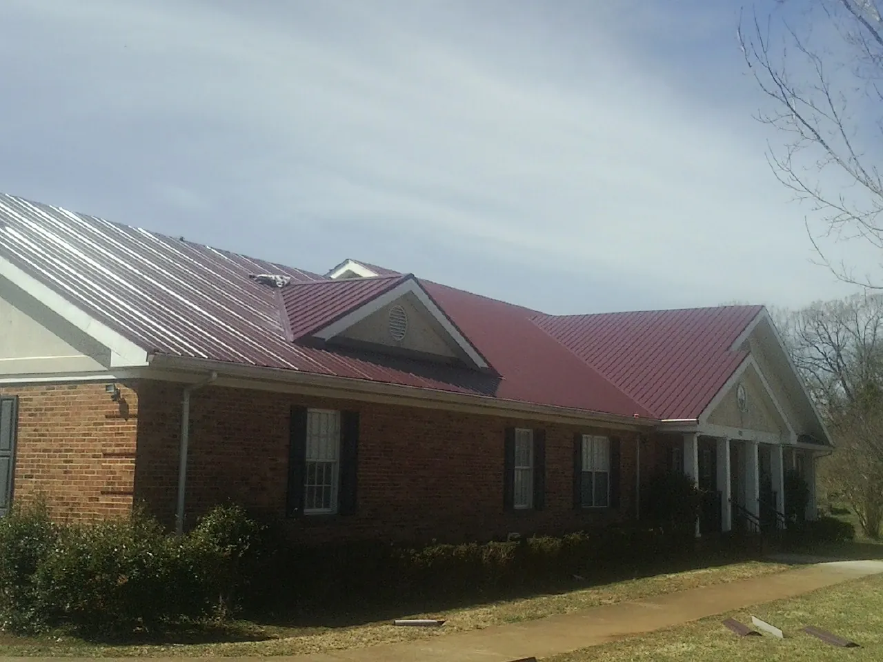 Red metal roof with gabled entries on a long brick building, from a Hail Damage Roof Repair job in Horseheads