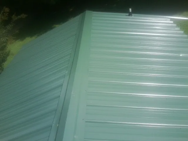 New green metal panels meeting at the ridge of a roof — Flat Roof Repair work by our crew in Horseheads