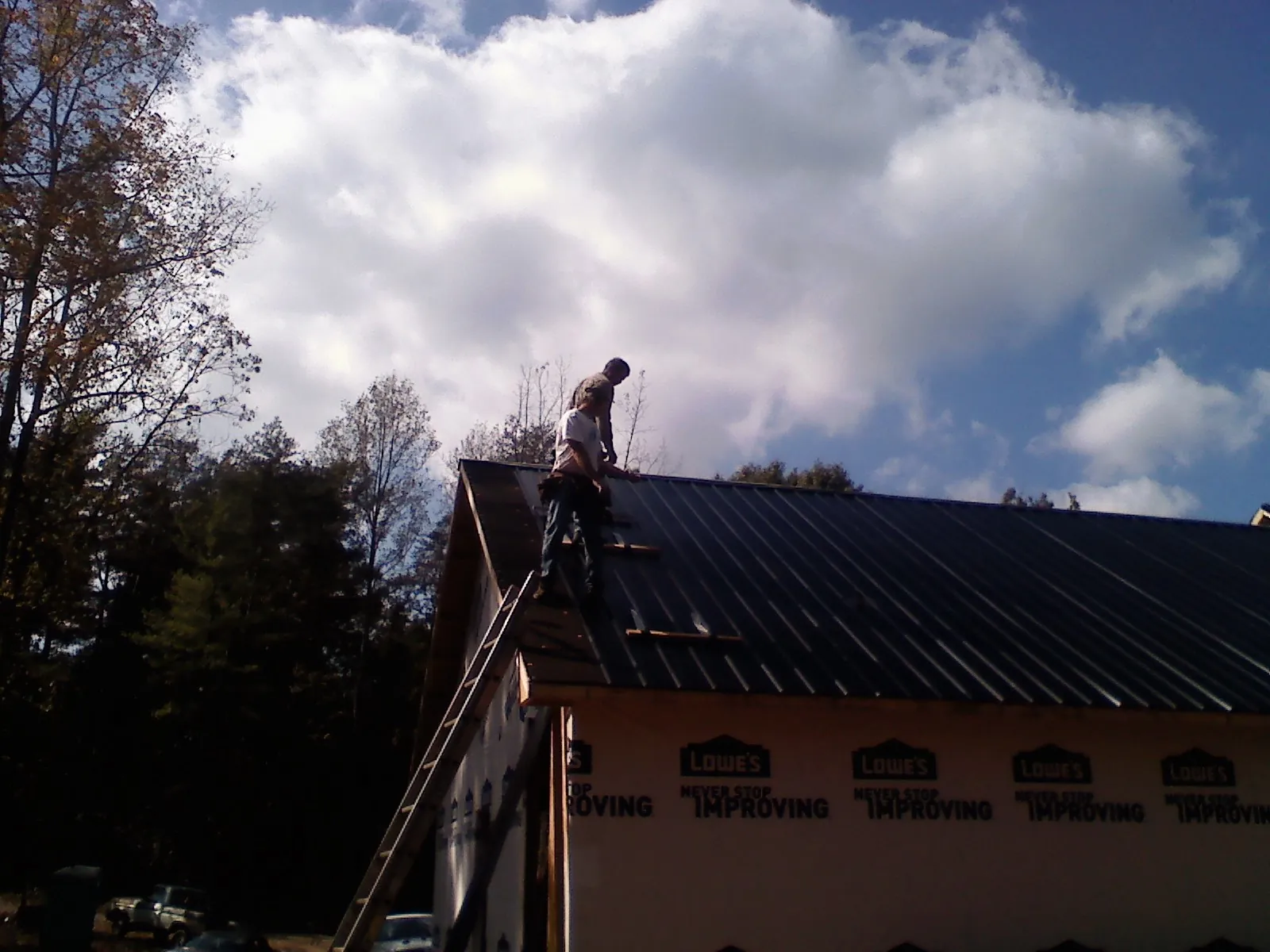 Roofer fastening dark metal panels high against a cloudy sky, from a Roof Inspection job in Horseheads