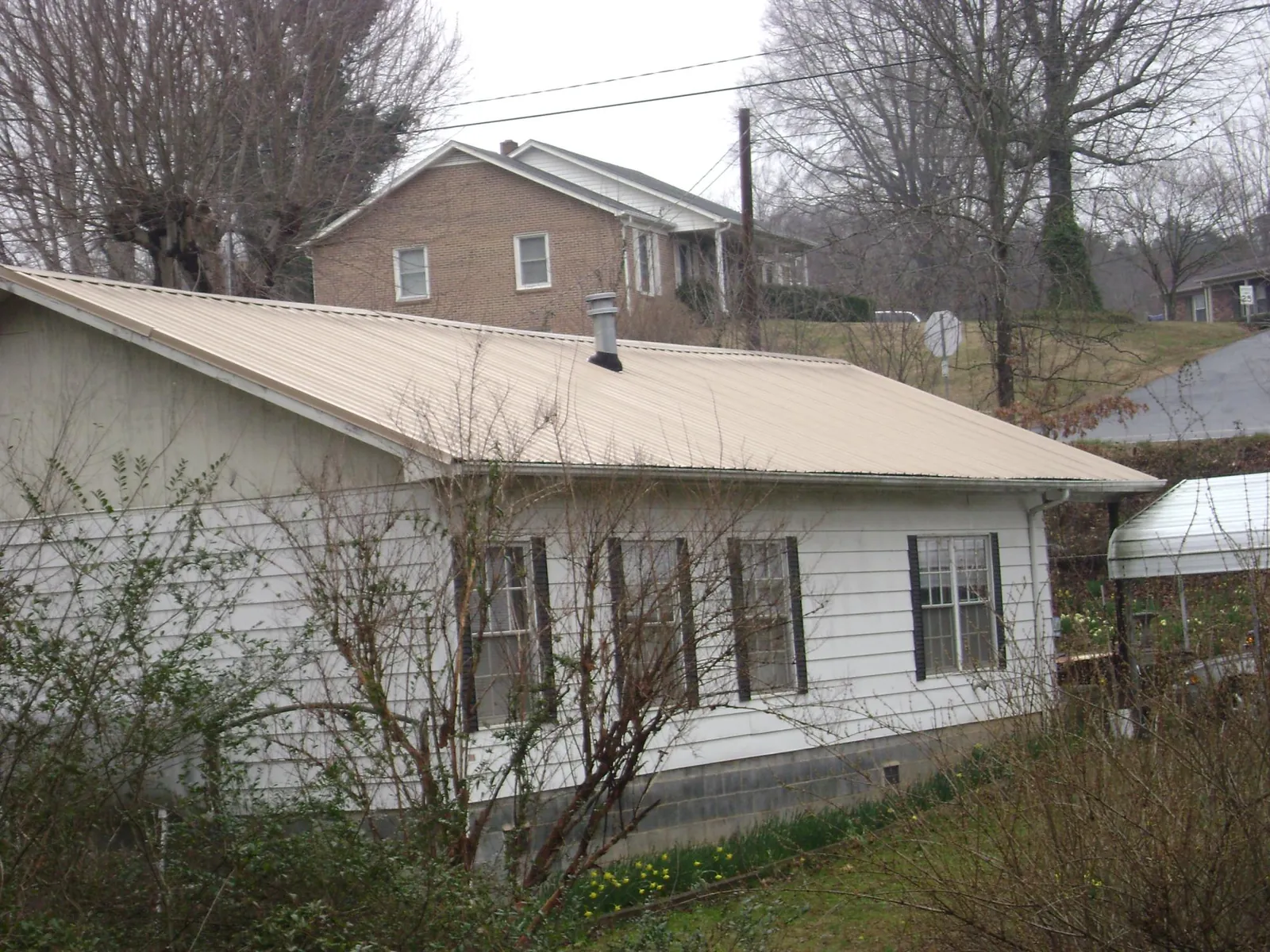 Tan metal roof on a white sided house set into a hillside — Commercial Roofing by Roofing Brothers in Horseheads